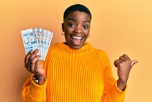 Young African American Woman Holding Peruvian Sol Banknotes Pointing Thumb Up To The Side Smiling Happy With Open Mouth