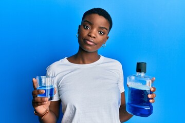 Sticker - Young african american woman holding mouthwash for fresh breath relaxed with serious expression on face. simple and natural looking at the camera.