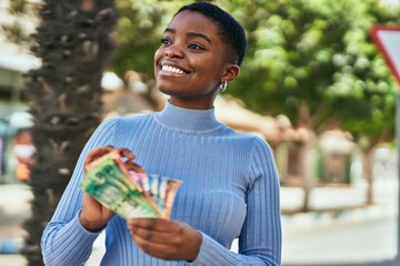 Poster - Young african american woman smiling happy counting south africa rand banknotes at the city.