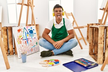 Poster - Young hispanic man at art studio sticking tongue out happy with funny expression. emotion concept.