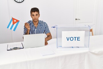 Sticker - Young handsome hispanic man at political campaign election holding cuba flag thinking attitude and sober expression looking self confident