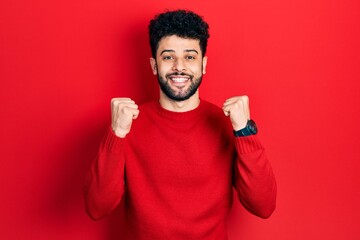 Poster - Young arab man with beard wearing casual red sweater celebrating surprised and amazed for success with arms raised and open eyes. winner concept.