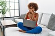Young african american woman sitting on the sofa at home using laptop smelling something stinky and disgusting, intolerable smell, holding breath with fingers on nose. bad smell