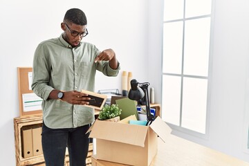 Poster - Young african american businessman unboxing box at the office pointing down with fingers showing advertisement, surprised face and open mouth