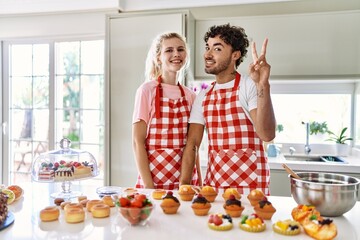 Poster - Couple of wife and husband cooking pastries at the kitchen showing and pointing up with fingers number two while smiling confident and happy.