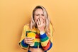 Beautiful young blonde woman drinking cup of coffee wearing headphones laughing and embarrassed giggle covering mouth with hands, gossip and scandal concept