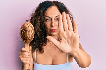 Poster - Middle age hispanic woman using comb with open hand doing stop sign with serious and confident expression, defense gesture