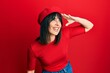 © Krakenimages.com - Young hispanic woman wearing french look with beret very happy and smiling looking far away with hand over head. searching concept.