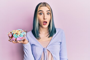 Wall Mural - Young modern girl holding bowl of sugar candy scared and amazed with open mouth for surprise, disbelief face