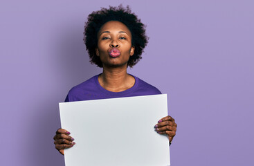 Poster - African american woman with afro hair holding blank empty banner looking at the camera blowing a kiss being lovely and sexy. love expression.