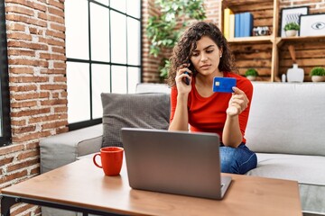 Canvas Print - Young latin woman talking on the smartphone using credit card and laptop at home