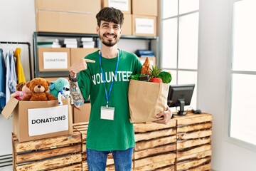 Poster - Hispanic man with beard wearing volunteer t shirt at donations point pointing finger to one self smiling happy and proud