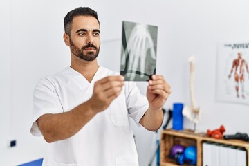 Canvas Print - Young hispanic man wearing physiotherapist uniform holding hand xray at clinic