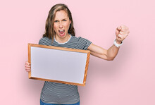 Young Blonde Woman Holding Empty White Board Annoyed And Frustrated Shouting With Anger, Yelling Crazy With Anger And Hand Raised
