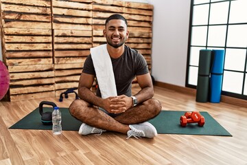 Poster - Young indian man sitting on training mat at the gym with a happy and cool smile on face. lucky person.