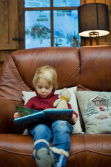 Poster - Blond toddler child, reading book and holding presents in a cozy cottage in the mountains