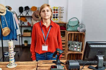 Poster - Middle age blonde woman working working as manager at retail boutique relaxed with serious expression on face. simple and natural looking at the camera.