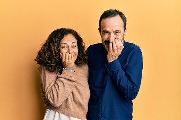 Sticker - Middle age hispanic couple wearing casual clothes laughing and embarrassed giggle covering mouth with hands, gossip and scandal concept