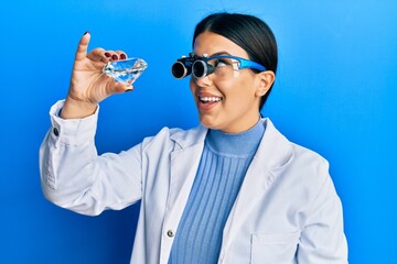 Poster - Beautiful brunette jeweller woman holding brilliant diamond stone wearing magnifier glasses smiling looking to the side and staring away thinking.