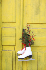 Wall Mural - Pair of ice skates with Christmas decor hanging on old yellow door