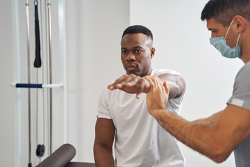 Wall Mural - Concentrated physiotherapist assessing muscle strength of young man