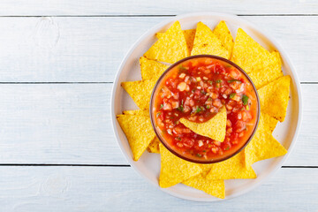 Wall Mural - Mexican salsa sauce and nacho chips on a white plate. Tortilla chips and salsa dip in bowl on white boards. Mexican food concept. Top view. Copy space