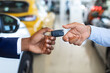 Closeup Of Black Car Seller Giving Keys To Male Customer In Showroom