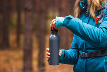 Hiker Opening Thermos Bottle With Hot Drink During Trekking In Forest. Camping And Refreshment During Hike In Woodland