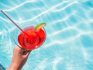 Wall Mural - Beautiful glass with a refresh cocktail and an attractive man on the background of the swim pool. Top view, close-up. Vacation and travel concept. Moments of celebration