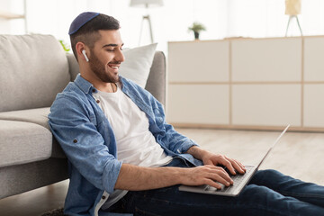 Young israeli male in kippa working on laptop at home