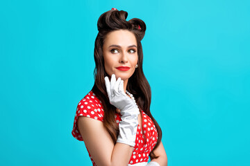 Beautiful pinup woman in red polka dot dress and gloves wearing bright makeup, looking aside on blue background