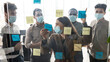 © Prostock-studio - Businesspeople in disposable masks brainstorming using post-it notes on wall