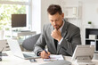 © Pixel-Shot - Thoughtful young businessman writing on clipboard at table in office
