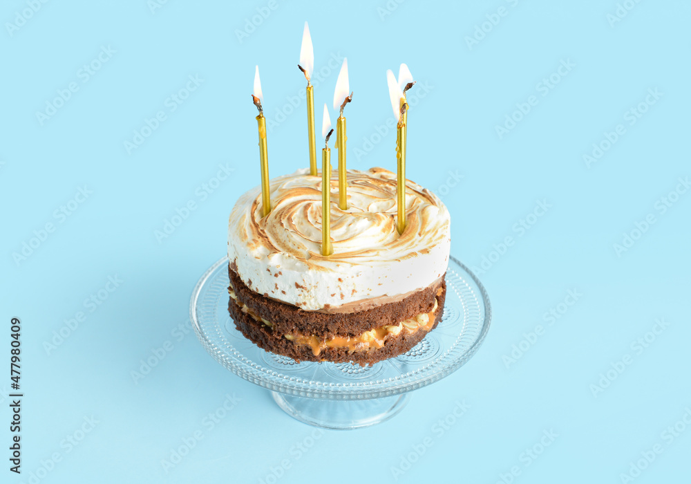 Stand with tasty birthday cake and burning candles on blue background