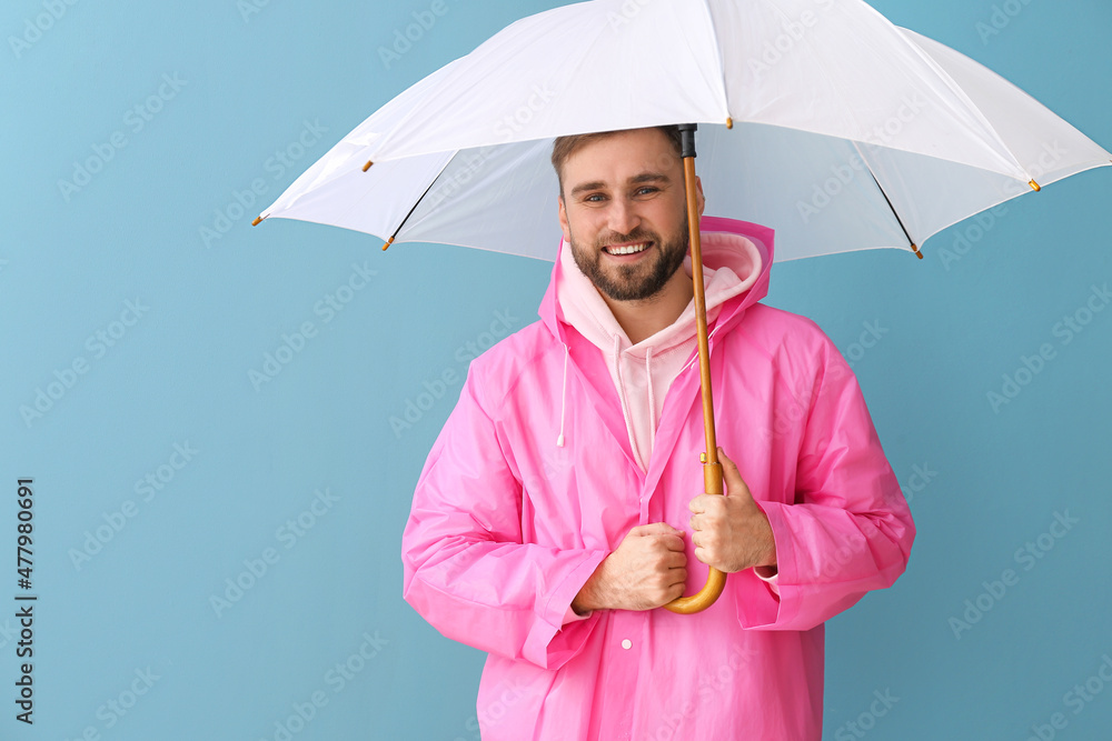 Young man in stylish raincoat and with umbrella on color background