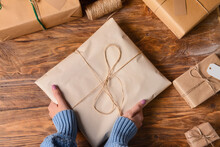 Woman In Warm Sweater Holding Wrapped Christmas Present On Wooden Background, Closeup
