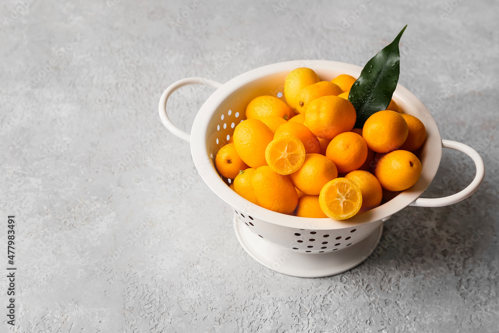 Colander with tasty kumquat fruits on light background