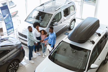 Above view of young black family shaking hands with car salesman, purchasing or renting new vehicle at auto dealership