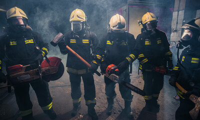 Wall Mural - Group of firefighters with  chainsaw and sledge hammer practicing in the garage of the fire department