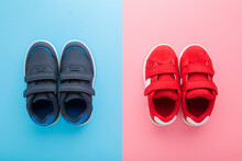 Red And Dark Blue Sport Shoes For Little Boy And Girl On Light Blue Pink Table Background. Pastel Color. Children Footwear. Closeup. Top Down View.