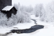 An Old Mill Covered With Snow By A Frozen River
