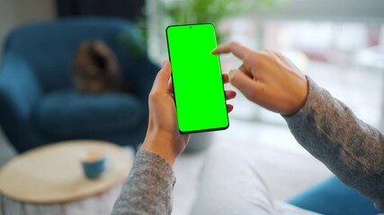 Woman at home using smartphone with green mock-up screen in vertical mode. Girl browsing Internet, watching content, videos. POV.