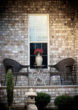 Romantically Arranged Lawn Chairs, Table And Red Flowers Vase In Front Of House Window.