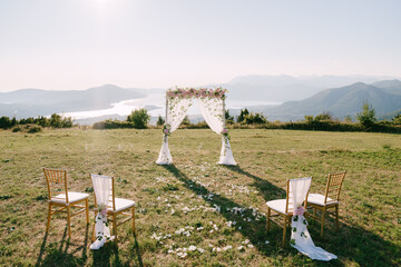 Wall Mural - Wedding arch decorated with flowers and curtains stands on the mountain in front of the chairs