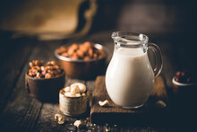 Vegan Alternative Non Dairy Milk From Nuts In A Jug With Various Nuts On Wooden Table