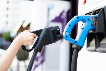 Unrecognizable Asian woman holding a DC - CCS type 2 EV charging connector at EV charging station.