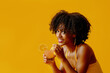 © Carlos David - beautiful young African american woman in bright summer outfit drinking refreshing cocktail isolated on yellow background