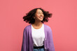 Portrait of smiling African American female model posing with healthy curly flying hair on pink studio background
