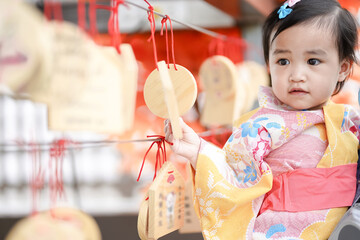 asian cute little girl in japanese traditional costume looking and holding a holy hanging wood in a 