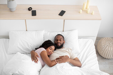 Wall Mural - Calm millennial african american female and male sleeping at night, hugging on bed in bedroom interior